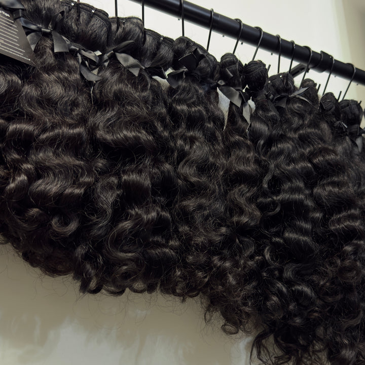 Raw Loose Curly hair bundles on rack  by Bundles and Drops of Glam 